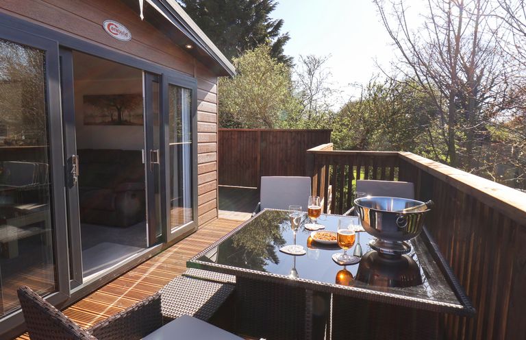 An outdoor wooden deck with a glass-top table and four chairs with drinks and snacks at Marigold Lodge in Runswick Bay near Staithes
