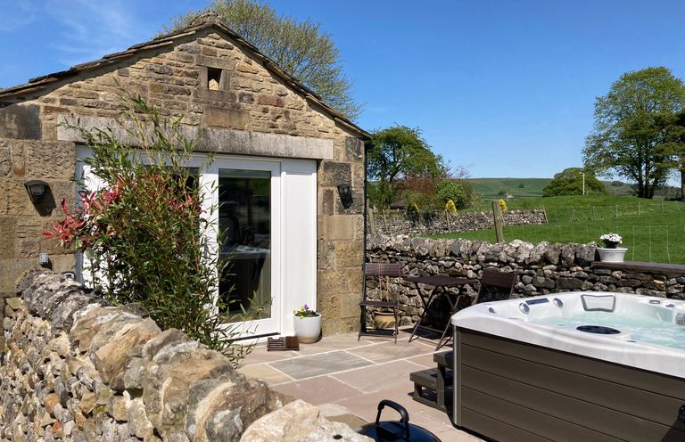 An outdoor patio with a stone wall a hot tub a small table with two chairs and a stone house at The Folly in Linton near Thresfield