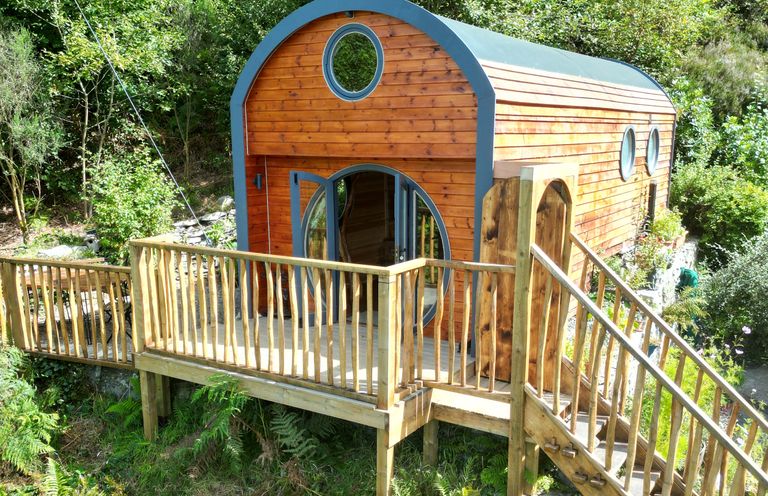 A wooden cabin with circular windows and a deck with a railing surrounded by greenery at The Kites Nest in Pont-rhyd-y-groes near Pontrhydfendigaid Snowdonia