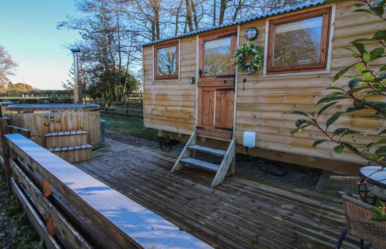 An outdoor wooden deck with a hot tub and a wooden cabin with a door and windows at The Oak Hut in Coton near Whitchurch