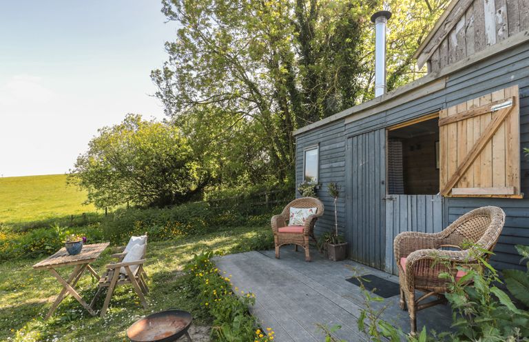 An outdoor seating area with wicker chairs and a wooden table next to a blue shed in a garden at The Snug in Dulverton