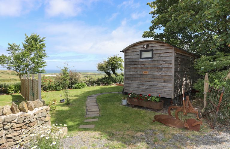A garden area with a wooden shed flowers on the ground a stone wall and distant ocean view at Shepherds Stone Llanfairynghornwy near Llanfaethlu