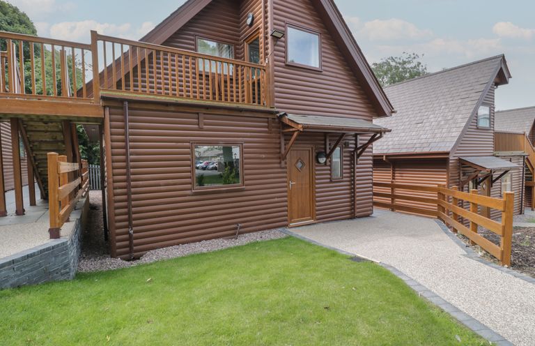 A brown wooden lodge with a grass lawn and a paved pathway at Classic Lodge 16 in Dyserth