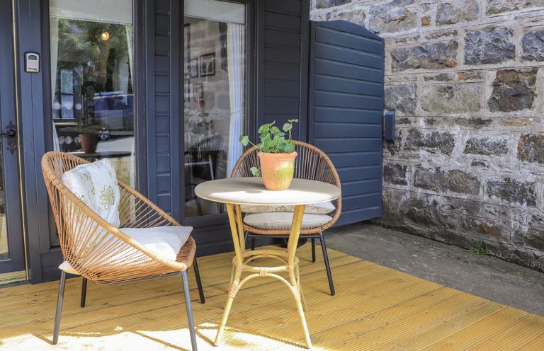 An outdoor patio with two wicker chairs with cushions a round table with a potted plant on a wooden deck at Creed Cabin in Stornoway