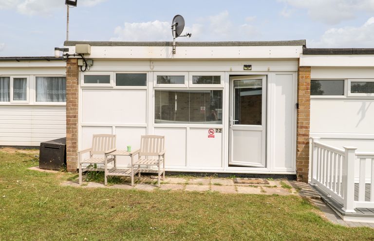 A small white building with two chairs and a table in front on a grassy lawn at 72 Hemsby