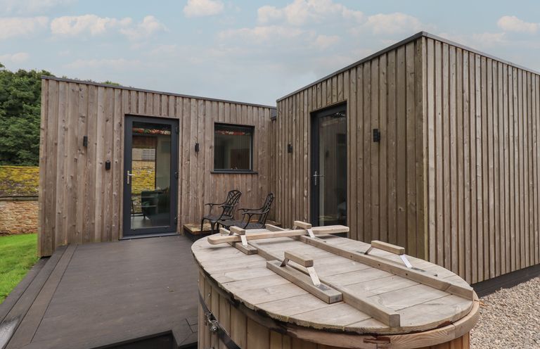 A wooden deck area with two metal chairs outside a cabin with vertical wooden panels and glass doors at Brow Wood Cabin in Ullswater