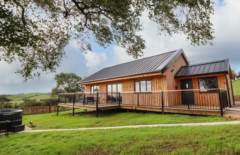 A wooden lodge with a metal roof and a wraparound deck on a grassy hill at Mynydd Y Glyn Lodge in Llanfyllin near Llanrhaeadr-Ym-Mochnant