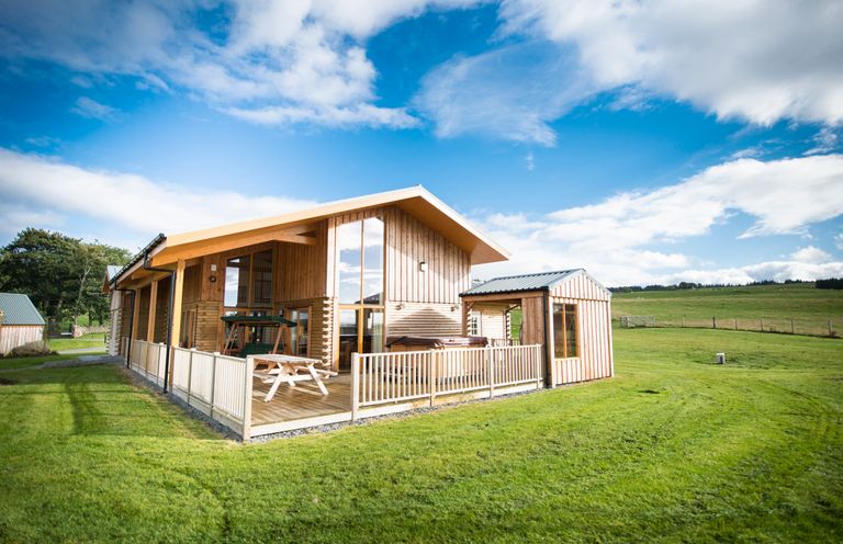 A wooden house with a fenced porch and picnic table on grass at Aurae in Cawdor near Inverness