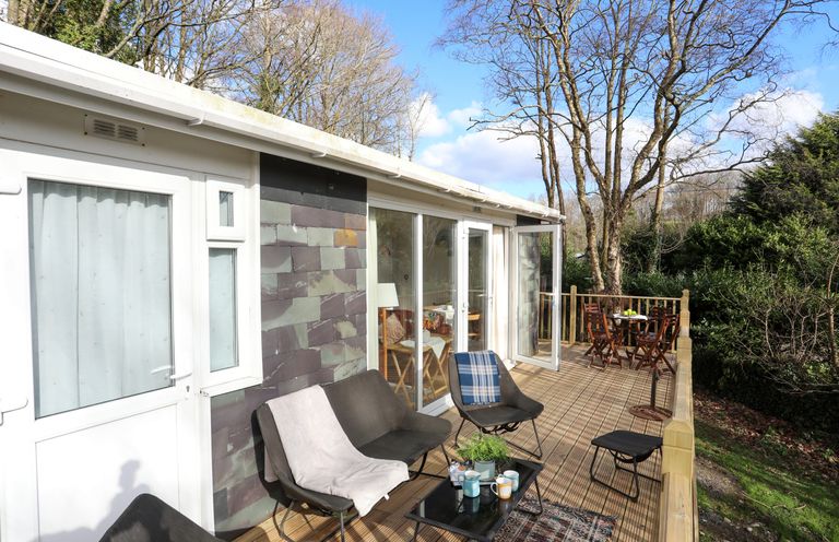 An outdoor wooden deck with chairs tables and a small plant at Treetops in Caernarfon