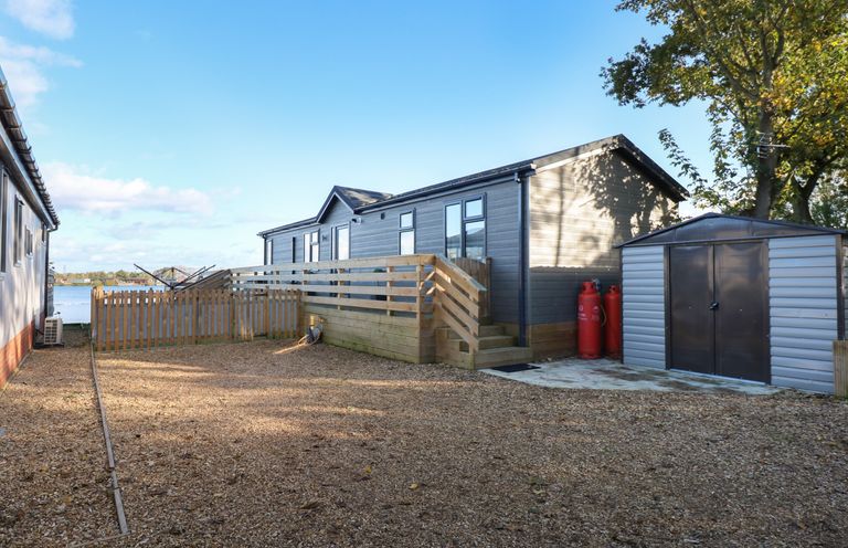 An outdoor area with a gravel ground a wooden decked mobile home two red gas cylinders and a metal shed at Lake View Lodge in Tallington