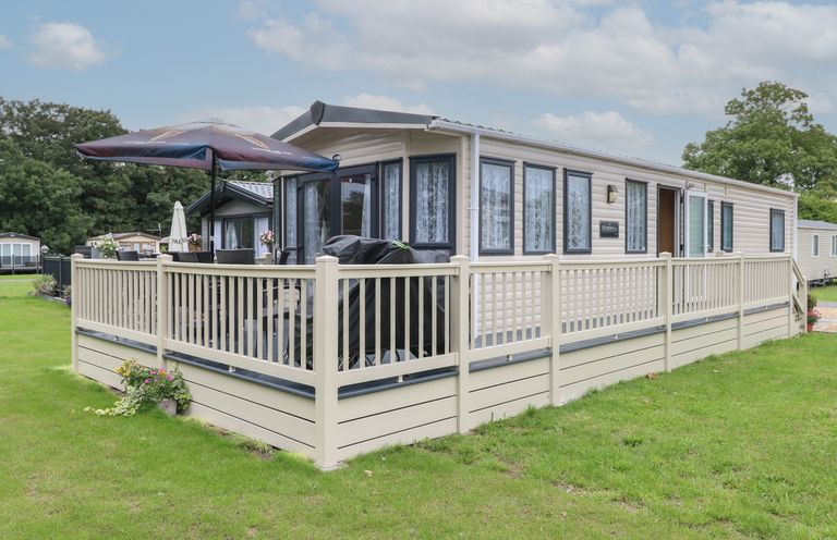 A mobile home with a fenced deck and outdoor furniture including an umbrella and grill at Stanley's Lodge Foxburrow Hang in Belton Norfolk