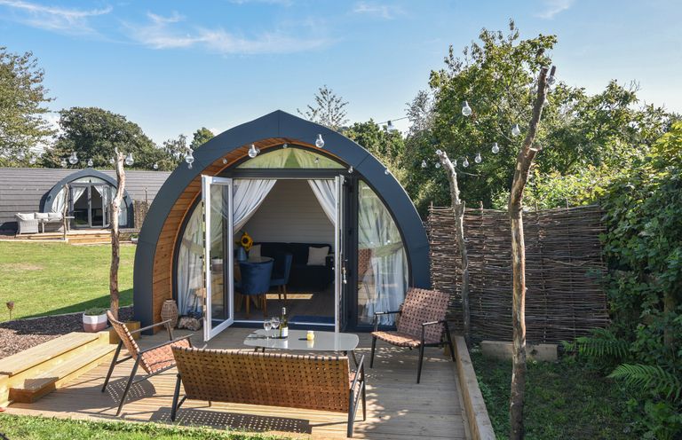A garden with a wooden deck patio set in front of an arched cabin with glass doors at Cedar in Wootton Fitzpaine near Charmouth