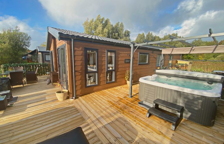 An outdoor wooden deck with a hot tub dining table chairs and a small house at Pine Lake View Coniston View 3 Carnforth