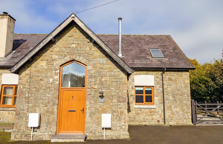 Stone house with wooden door and window under a pitched roof at School Lodge in Llandeilo