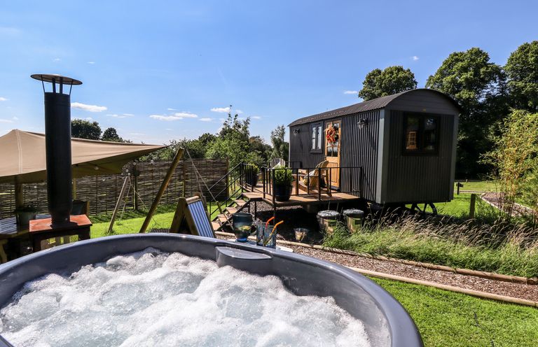 An outdoor area with a bubbling hot tub a small elevated cabin and lawn at Southdown Luxury Glamping in Nottingham