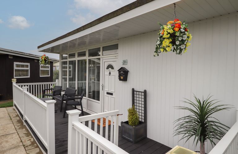 A porch with white railing black chairs hanging flower baskets and potted plants at 39 Cherry Park in Chapel St Leonards