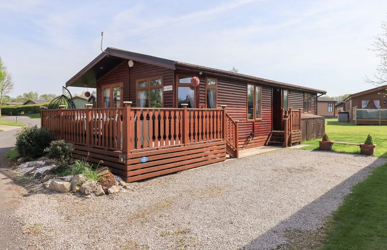 A wooden cabin with a fenced porch and gravel driveway at Our Happy Place Lakeside 16 Borwick near Carnforth