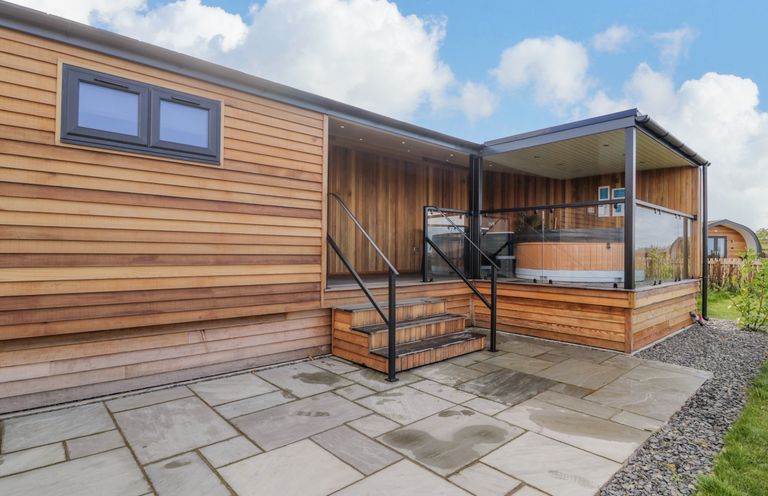 An exterior view of a wooden lodge with steps leading to a covered porch with glass railings at Betsi Lodge 1 in Llanelidan near Corwen