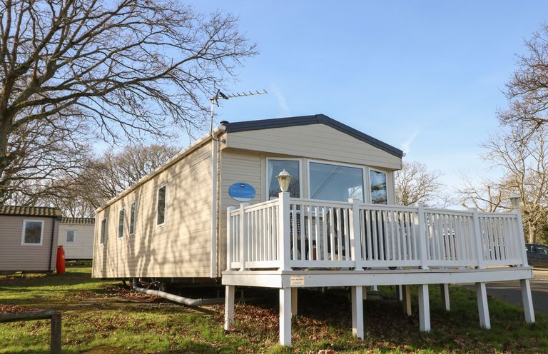 A static caravan with a white wooden deck surrounded by trees at 15 Rosewood Great Thorness near Northwood Isle Of Wight