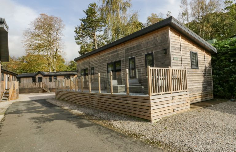 A wooden cabin with a deck and glass railing surrounded by trees at The Bothy in Keswick