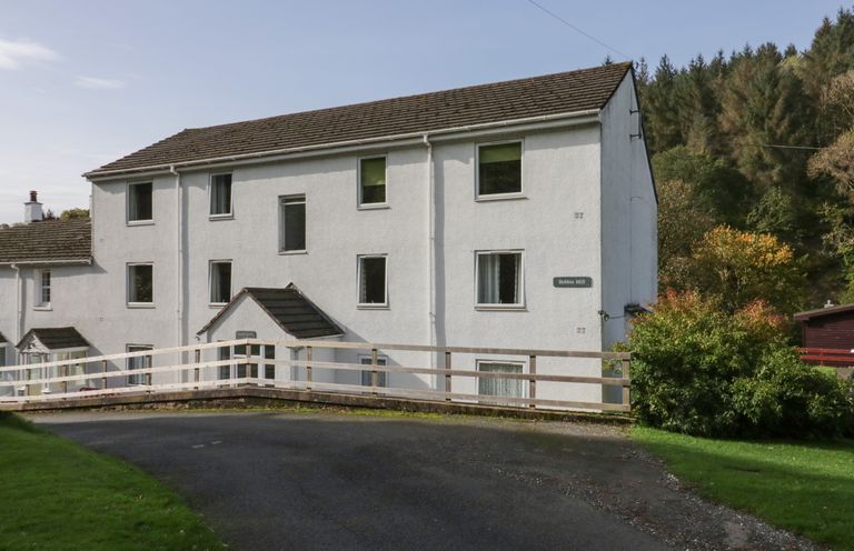 A white multi-story building with multiple windows and a sloped roof surrounded by trees at Apartment 2 in Keswick