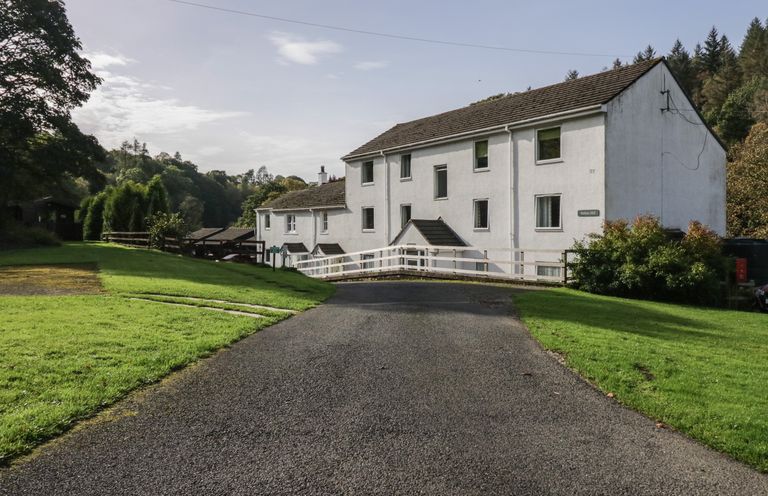 A white multi-story building with a sloped roof surrounded by grass and trees at Apartment 6 in Keswick