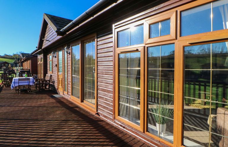 A wooden deck with outdoor furniture and table near a log cabin with large windows at The Fairhaven in Tunstall near Catterick North Yorkshire