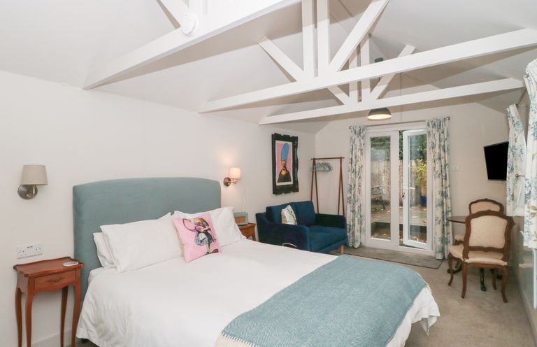 A bedroom with a bed a blue headboard a blue sofa chairs and a small table at The Potting Shed in Combe near Langport
