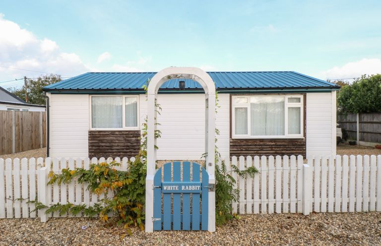 A small house with a blue roof behind a white picket fence and a blue gate with an arch at White Rabbit Cross Lane in Eccles-On-Sea