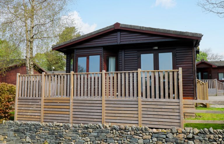 A wooden cabin with a fenced porch and stone wall in front at Hill Lodge in Applethwaite 2 Limefitt Park near Windermere