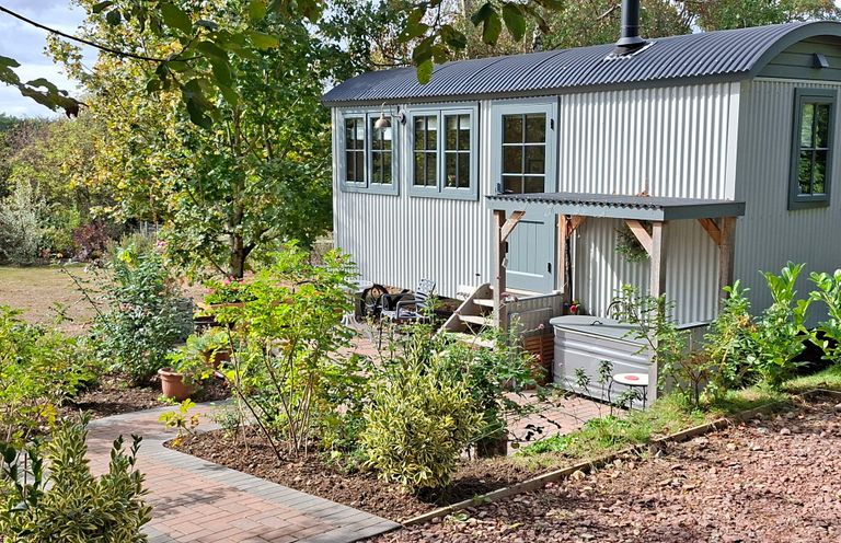 A shed with windows and chimney surrounded by garden at Evendine Hut @ Evendine Cottage, Colwall, Herefordshire