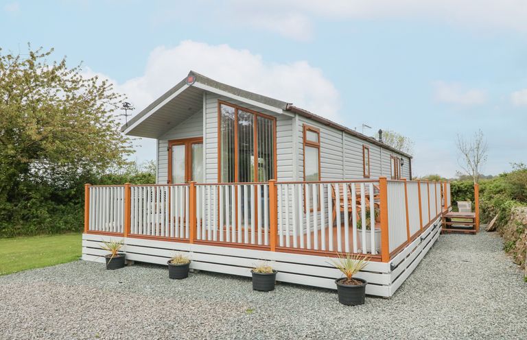 A single mobile home with wooden deck and potted plants on gravel at Y Caban in Brynsiencyn