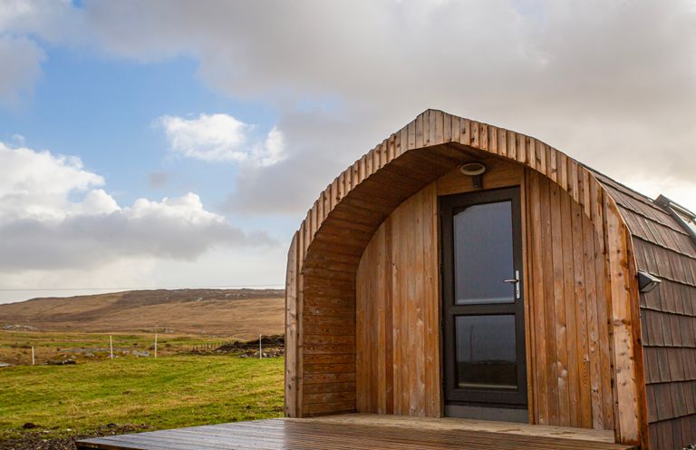 A wooden pod with a glass door on a deck in a grassy landscape at Heisgeir Sollas Isle Of North Uist