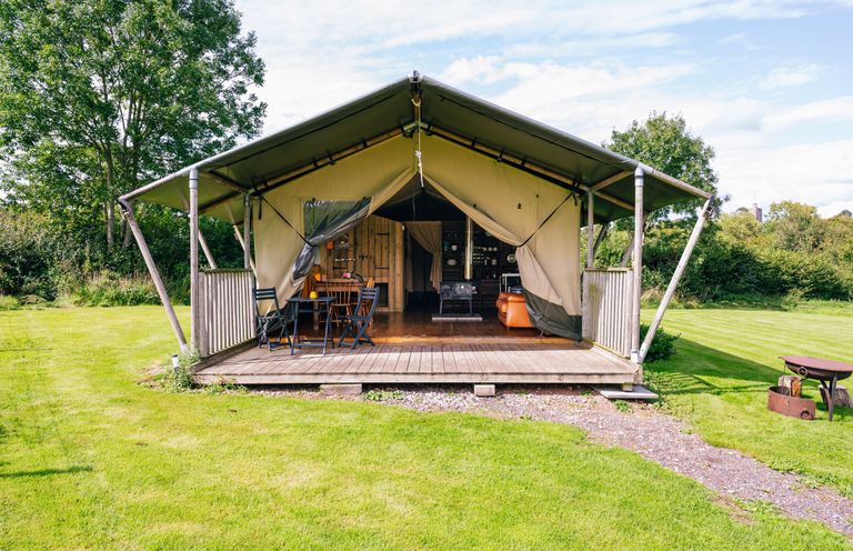 An outdoor tent with a wooden deck table and chairs surrounded by grass and trees at Oak Stockland near Dalwood