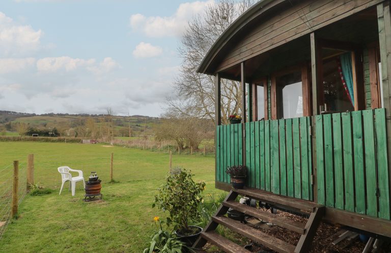 A wooden hut with green fence and steps leading to the door on a grassy field with a white chair and kettle on an outdoor stove at Harri's Hut in Bishop's Lydeard