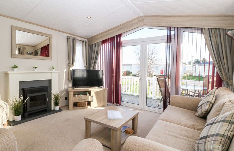 A living room with a fireplace TV sofa coffee table and glass doors leading outside at Snape Lodge Towyn