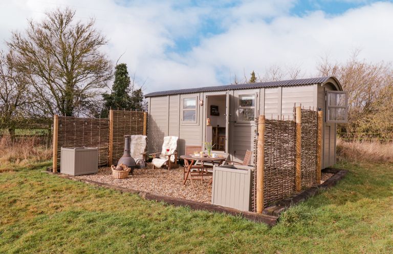 An outdoor seating area with wooden chairs and table near a small cabin with woven fences around it at Bumble's Retreat in Whepstead near Bury St Edmunds