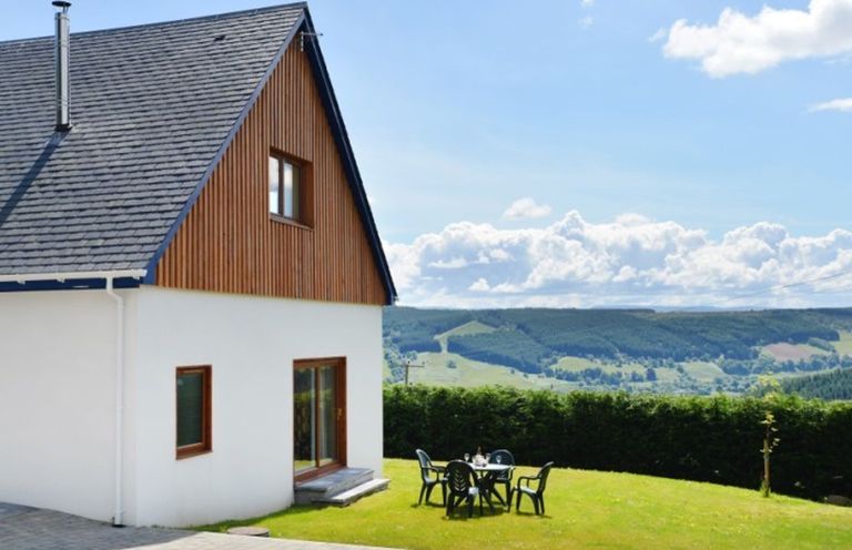 A house with a sloped roof and wooden paneling next to a grassy yard with plastic chairs and a table at Glen View Lodge in Drumnadrochit Loch Ness