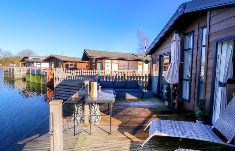 Decking area with outdoor seating and a table beside water at Gressingham 7 in Warton near Carnforth