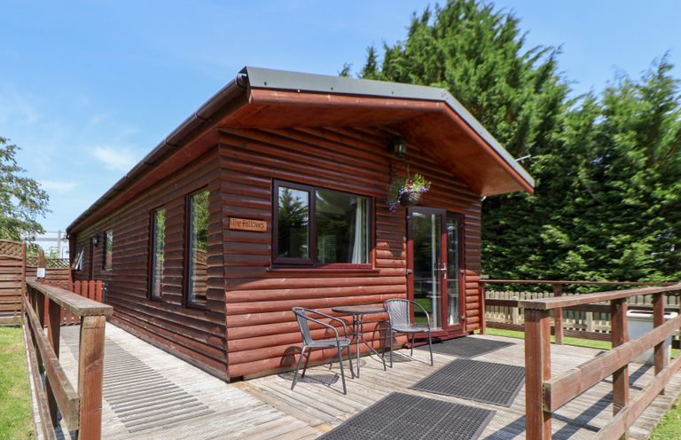 A wooden cabin with a deck and chairs at The Fallows Llanerch Park near St Asaph