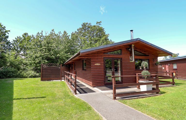 A log cabin with a pathway and grassy area at The Roe Llanerch Park near St Asaph