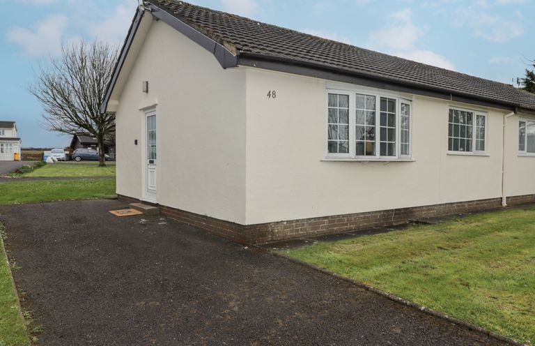 A single story house with a driveway and grass lawn at 48 Gower Holiday Village in Scurlage