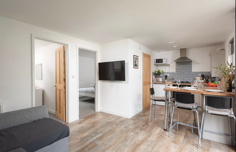 An open living and kitchen area with a wall-mounted television wooden doors and a breakfast bar with chairs at Wheal Prosper Lodge in Wendron near Helston