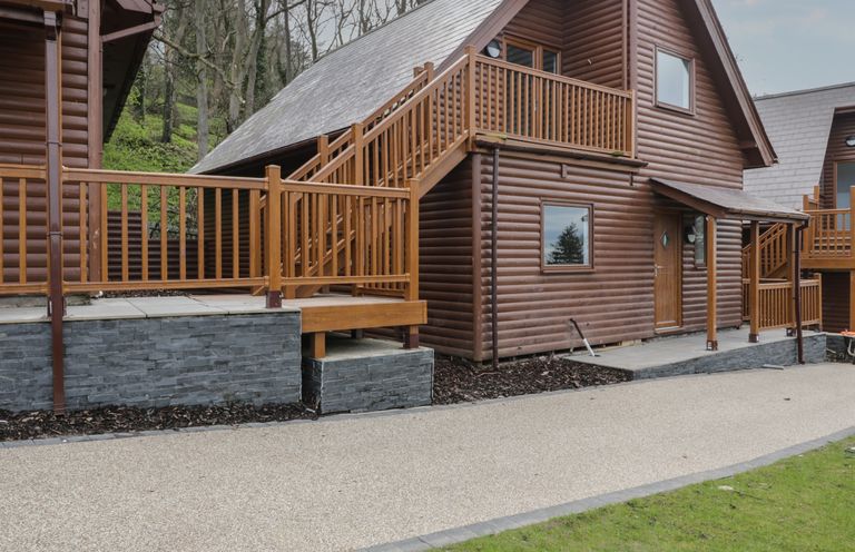 A wooden cabin with an external staircase and railing surrounded by trees at Premier Lodge 41 in Dyserth