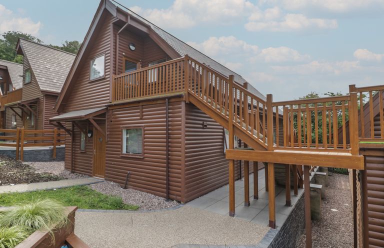 A wooden cabin with an outdoor staircase and railing leading to an upper door at Classic Lodge 15 in Dyserth