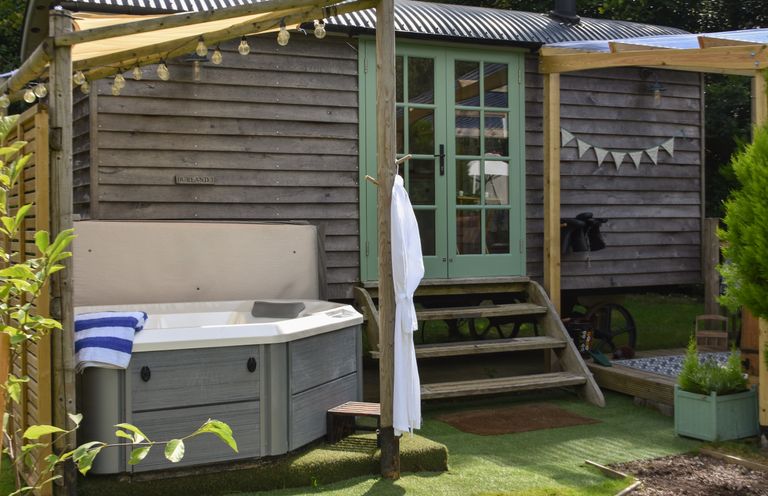 An outdoor area with a hot tub and wooden steps leading to a structure with green double doors at Burr 1 Shepherds Hut in Barnstaple