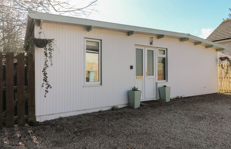 Front view of a white single-story building with two windows and a glass-paneled door with plants in pots at the entrance at Caldwell Cottage in Lanark