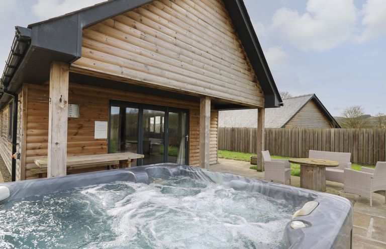 An outdoor patio with a hot tub wooden table bench and wicker chairs at Caban Dulas in Rhayader