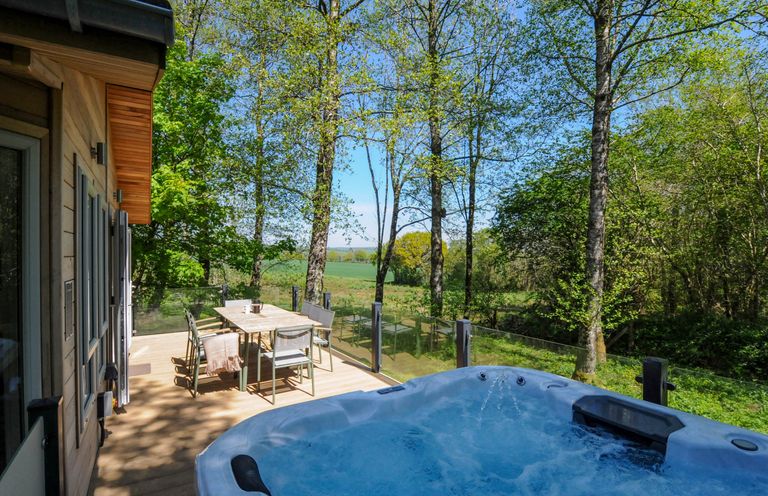 An outdoor deck with a hot tub and a dining table surrounded by trees at 23 Meadow Retreat in Dobwalls