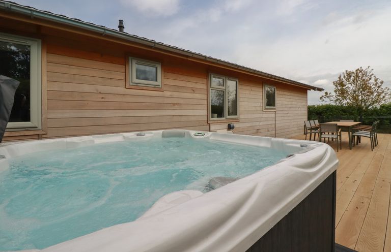 An outdoor wooden deck with a hot tub and a dining table with chairs at 6 Faraway Fields in Dobwalls